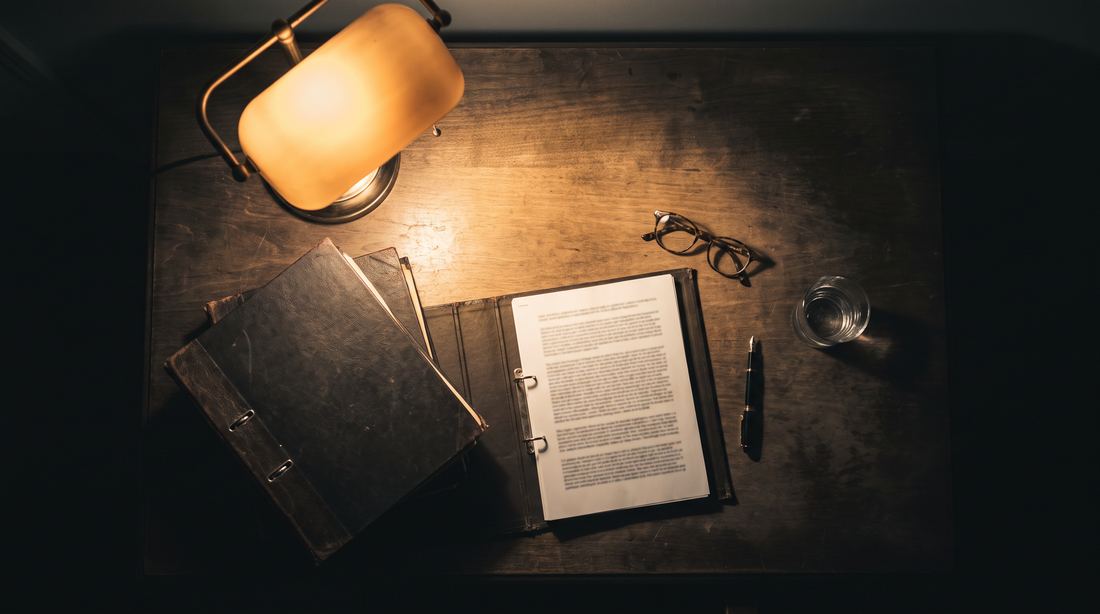 Schreibtisch bei Nacht mit Aktenordnern und aufgeschlagenen Unterlagen